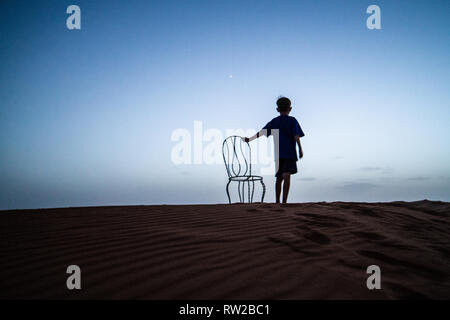 Garçon avec une chaise dans le désert la nuit, Merzouga, Maroc Sahara - dunes de l'Erg Chabbi Banque D'Images