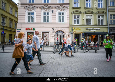 Les gens qui marchent le long des rues pavées de la place du marché principale de Cracovie-w vieille ville avec boutiques derrière eux, Lesser Poland Voivodeship, Pologne. Banque D'Images