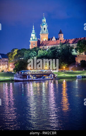 Les feux fonctionnent le grand château royal de Wawel la nuit avec ferry amarré le long de la rivière Vistule, Krak-w, Lesser Poland Voivodeship, Pologne. Banque D'Images