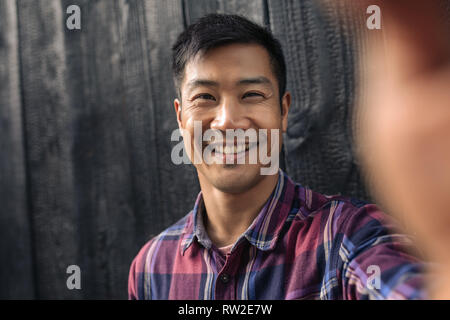 Smiling Young Asian man appuyé contre un mur en tenant vos autoportraits Banque D'Images