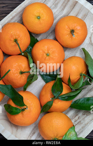 Matières premières fraîches et de mandarines avec des feuilles vertes. Aspect rustique. Sur fond de bois. Banque D'Images