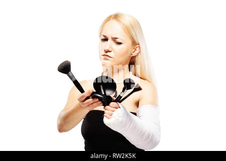 Fille blonde avec un bras cassé dans le plâtre de la difficulté à mettre un miroir Banque D'Images