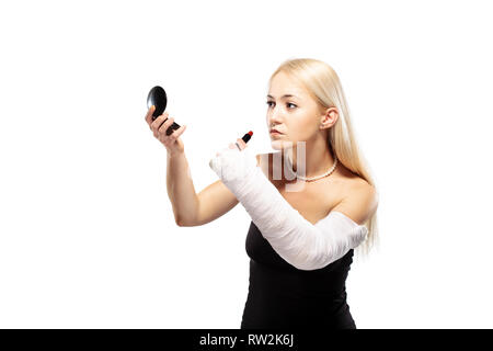 Fille blonde avec un bras cassé dans le plâtre de la difficulté à mettre un miroir Banque D'Images