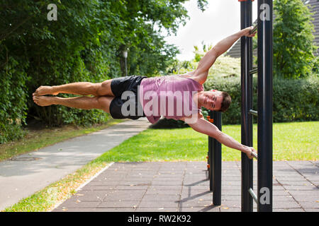 Jeune homme de faire les exercices sur la barre verticale à l'extérieur dans le parc, l'exécution figure drapeau humain. Banque D'Images