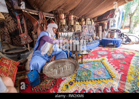 Homme portant un turban et berbère deraa sort théière en préparation de la cérémonie du thé traditionnel Marocain, Maroc, Oasis Tighmert Banque D'Images