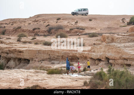 Les gens se rafraîchir dans un canal d'eau dans le paysage aride de l'Oasis de Tighmert, Maroc Banque D'Images