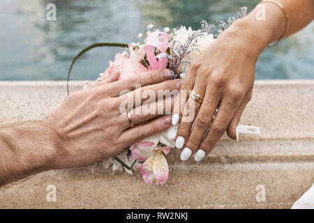 Jeunes mariés montrant les anneaux de mariage sur le dessus du bouquet, jour du Outdoor Banque D'Images