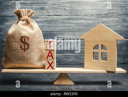 Maison en bois et un sac d'argent avec le mot taxe sur les échelles. Les taxes sur l'immobilier, le paiement. Registre des contribuables pour la propriété. Citoyen respectueux des lois. Banque D'Images