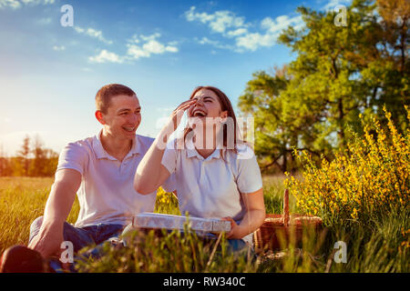 Happy laughing couple eating pizza à l'extérieur. La femme et l'homme having picnic au coucher du soleil. Les gars sortir ensemble et s'amuser. Banque D'Images