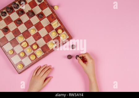 Kid mains sur un échiquier jouant aux échecs sur fond rose, vue du dessus Banque D'Images