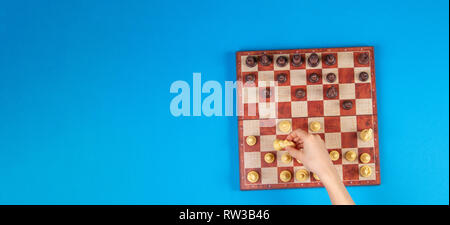 Kid mains sur un échiquier jouant aux échecs sur fond bleu, vue d'en haut Banque D'Images