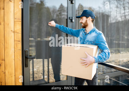 Delivery man knocking porte de la maison moderne, la prestation de certains biens dans la parcelle de papier accueil Banque D'Images