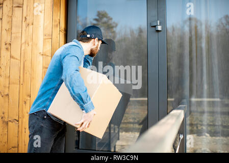 Delivery man à l'intérieur de la maison moderne, la prestation de certains biens dans la parcelle de papier Banque D'Images