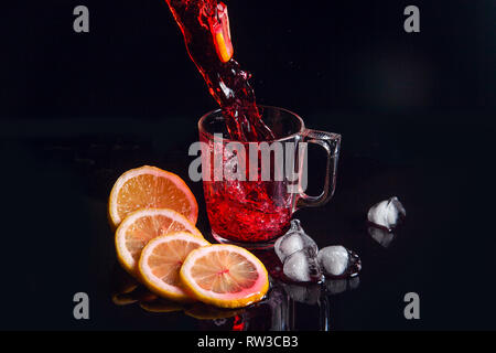 Boisson glacée de l'été - hibiscus thé froid avec de la glace, citron et menthe. Hibiscus thé froid et verser dans le verre avec de la glace réfléchissante isolé sur la surface noire. Bonjour Banque D'Images