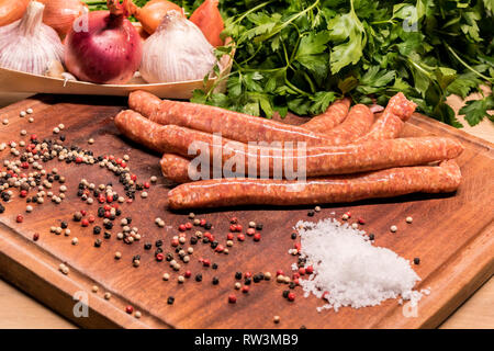 Les saucisses crues avec du chili et des herbes sur une planche en bois avec des épices Banque D'Images