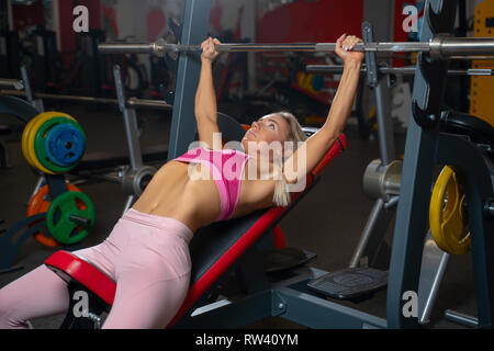 Jeune fille blonde allongé sur banc avec barbell. Banque D'Images