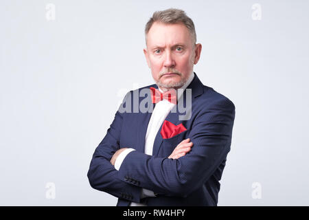 Senior businessman en costume bleu nous regarde sur fond gris. Banque D'Images