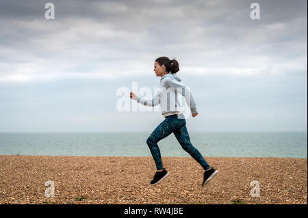 Femme en marche le long d'une plage de galets de la mer, se tenir en forme. Banque D'Images