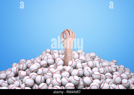 Man's hand holding a baseball, sortant de sous un gros tas de base-ball. Banque D'Images