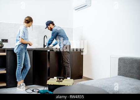 Plombier bricoleur ou la réparation du robinet de cuisine avec jeune femme dans l'appartement. Accueil concept service de réparation Banque D'Images