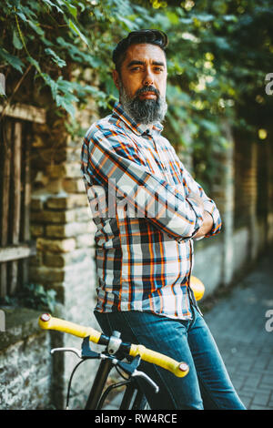 Un beau jeune homme va à la ville avec son vélo, debout à côté d'elle et d'attendre que quelqu'un. Banque D'Images