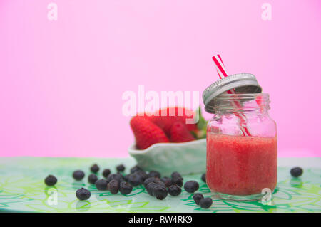 Un jus de fraises fraîches dans un bocal à côté des bleuets et fraises entières. Le fond rose avec l'espace pour ajouter des textes (copie espace) Banque D'Images