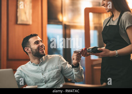 Un beau jeune homme est payant de serveuse pour café avec carte de crédit dans un café. Banque D'Images