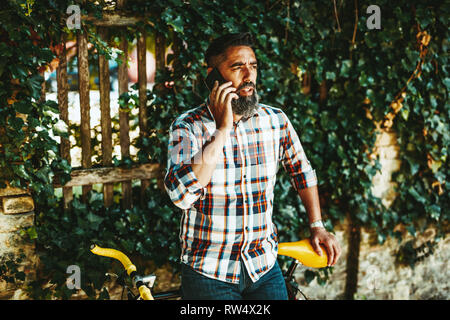 Un beau jeune homme va à la ville avec son vélo, debout à côté d'elle, l'attente de quelqu'un et parler sur le smartphone. Banque D'Images