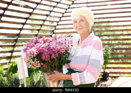 Jardinier Senior posant avec des fleurs Banque D'Images