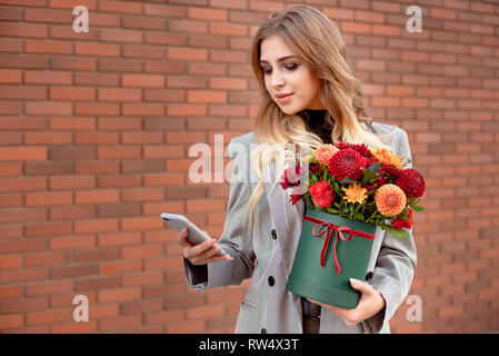 Belle jeune fille cherche dans le téléphone dans ses mains tenant une boîte verte avec des couleurs vives Banque D'Images