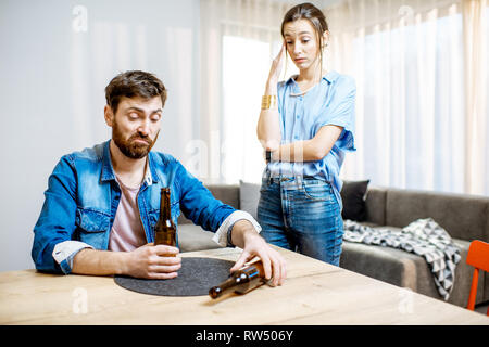 Ivre l'homme souffrant d'alcoolisme déprimé assis à la maison avec jeune femme dans le désespoir sur l'arrière-plan Banque D'Images