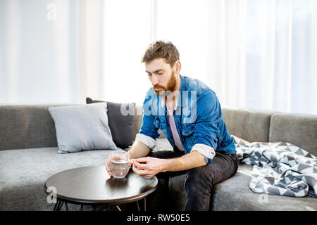 L'homme certains médicaments se sentir mal ou d'avoir la gueule de bois après l'alcool, assis sur le canapé à la maison Banque D'Images