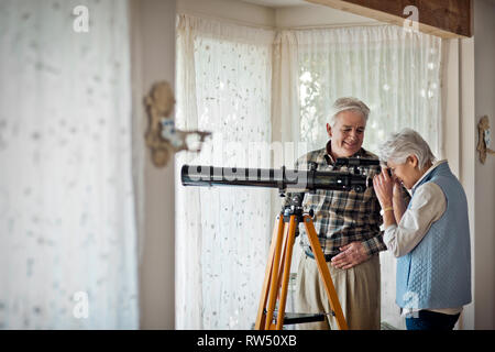 Couple à l'aide d'un télescope dans leur salon. Banque D'Images