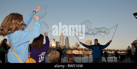 Les enfants chasse et bulles qui faites par l'artiste de rue sur la rivière Thames Embankment, London, UK. Banque D'Images