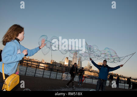 Les enfants chasse et bulles qui faites par l'artiste de rue sur la rivière Thames Embankment, London, UK. Banque D'Images