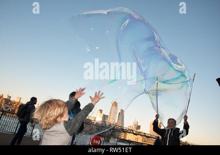 Les enfants chasse et bulles qui faites par l'artiste de rue sur la rivière Thames Embankment, London, UK. Banque D'Images