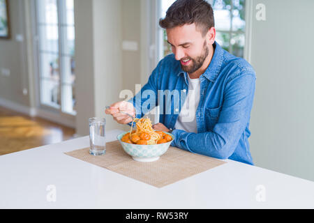 Bel homme de manger des pâtes avec des boulettes de viande et de la sauce tomate à la maison tout en souriant à l'appareil photo Banque D'Images