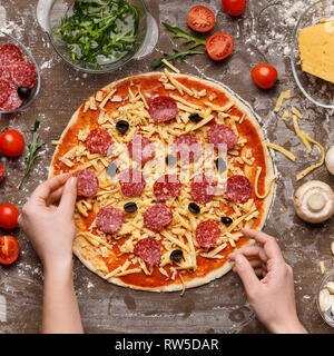 Woman putting on pizza salami, vue du dessus Banque D'Images