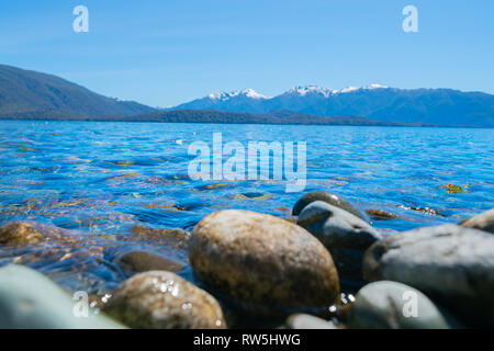 Surface de l'eau et le lac Stony flou artistique bord de lac Te Anau sous ciel bleu avec des montagnes au loin Banque D'Images