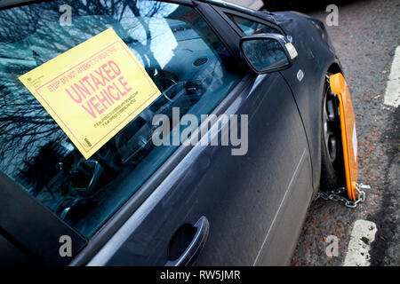 L'étiquette d'avertissement et de la roue du véhicule non taxés sur collier de serrage voiture sur une rue au Royaume-Uni Banque D'Images