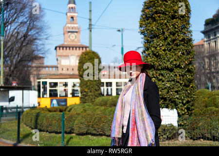 Mannequin posent avec une écharpe rouge har, et manteau noir pour un portrait avec Castelo Sforzesco de Milan à l'arrière-plan dans une journée ensoleillée Banque D'Images