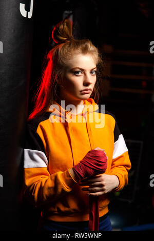 Femme blonde en boxer noir jaune rouge tire des bandages sur ses mains sur fond noir Banque D'Images
