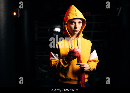 Jeune femme en boxer rouge tire du capot des bandages sur les mains sur fond noir Banque D'Images