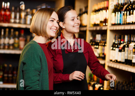 Photo de deux femmes souriant sur fond flou d'étagères avec des bouteilles de vin en magasin Banque D'Images