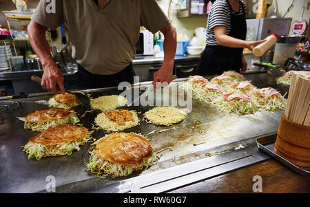 De style japonais d'Hiroshima okonomiyaki salés crêpes farcies de yakisoba nouilles sont préparés par deux chefs sur une grande plaque. Banque D'Images