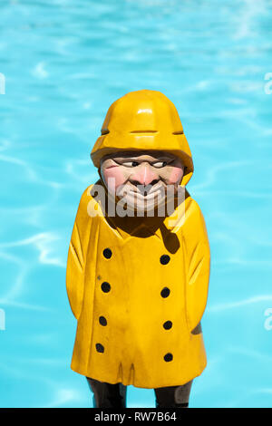 Pêcheur figure en bois avec manteau de pluie jaune et tuyau à fumée sur fond piscine Banque D'Images