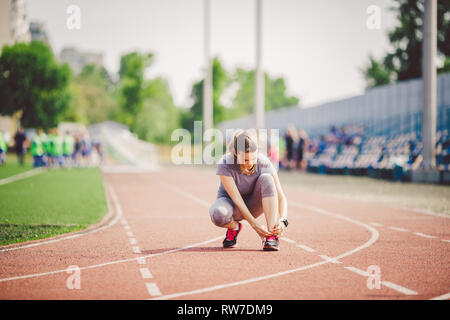 Thème les sports et sportswear. Une jeune femme de race blanche en uniforme le laçage des lacets de chaussures sport réglage de voie sur un tapis roulant dans un stade. Banque D'Images