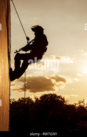 Silhouette d'un agent de police pendant les exercices de corde avec des armes. Banque D'Images