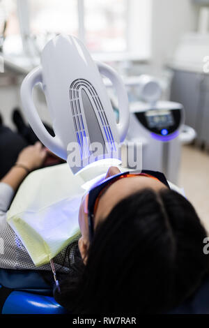 Patient avec des lunettes de sécurité et de l'enrouleur sur la joue. Lampe lumière laser activer comme une procédure de blanchiment des dents professionnels. Women's Cosmet Banque D'Images