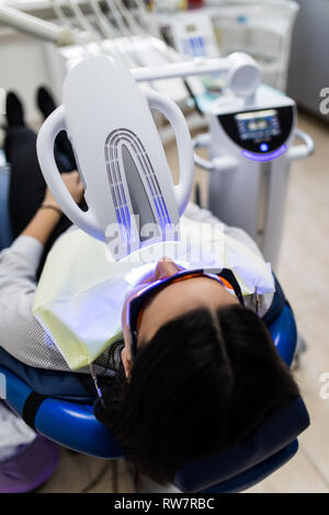 Patient avec des lunettes de sécurité et de l'enrouleur sur la joue. Lampe lumière laser activer comme une procédure de blanchiment des dents professionnels. Women's Cosmet Banque D'Images